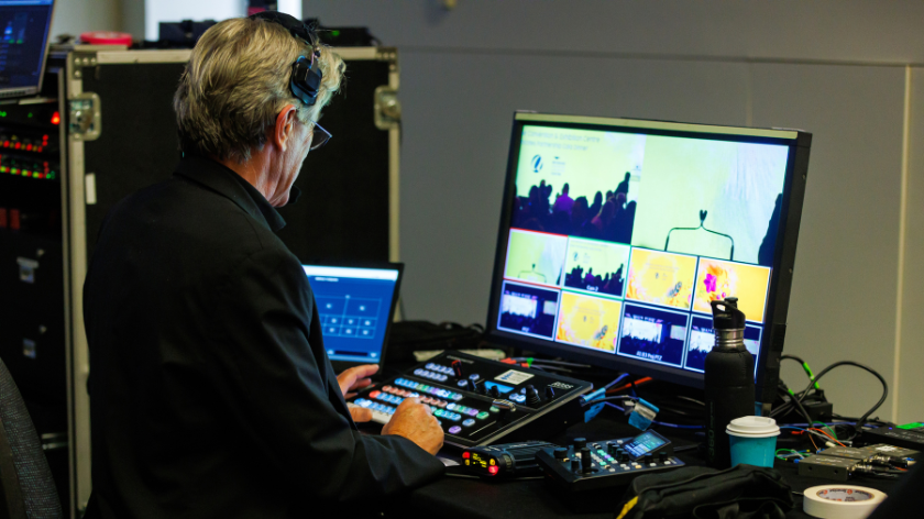 Image of an AV team member operating equipment controlling the display of the event screens and cameras capturing the room