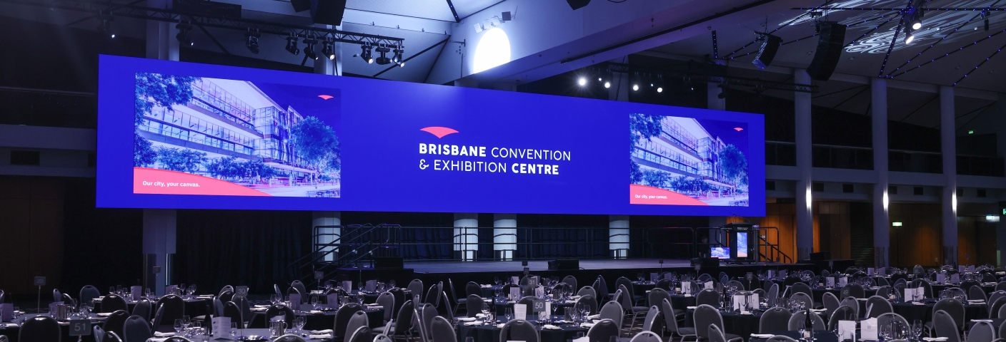 Image of the Plaza Ballroom wide-format LED screen, spanning 24 meters and displaying the Brisbane Convention & Exhibition Centre logo on a dark blue background with exterior images of the venue either side.