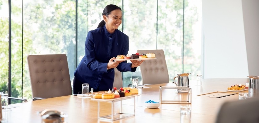 Boardroom with floor to ceiling windows allowing the space to be filled with natural light. Plates of small desserts are being served.