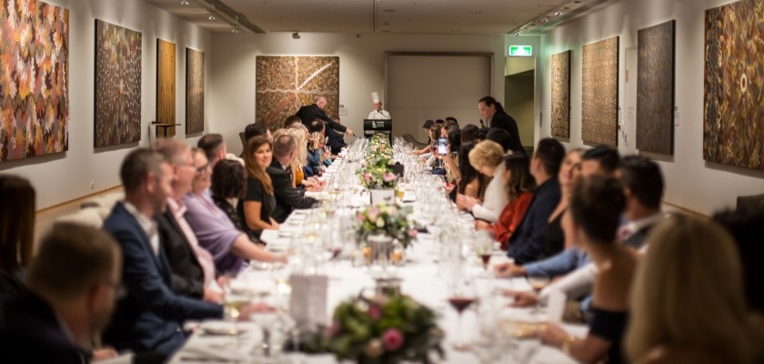 The Plaza Gallery hosting approximately 40 guests enjoying an intimate dinner party. The walls are lined with Indigenous artwork.