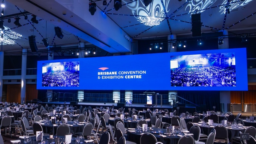 Image of the Plaza Ballroom LED screen, a wide-format screen spanning 24 meters. The screen displays the Brisbane Convention & Exhibition Centre logo centered with images either side capturing live footage of the banquet set room.