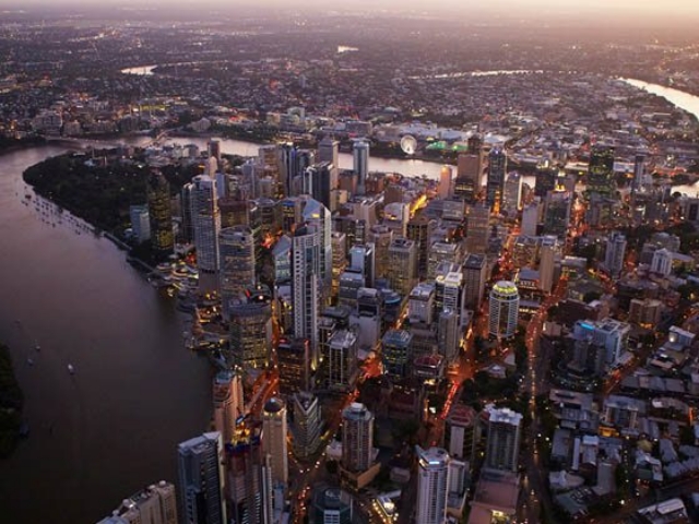 The cityscape of Brisbane unfolds with its river snaking through the dense urban landscape as twilight descends.